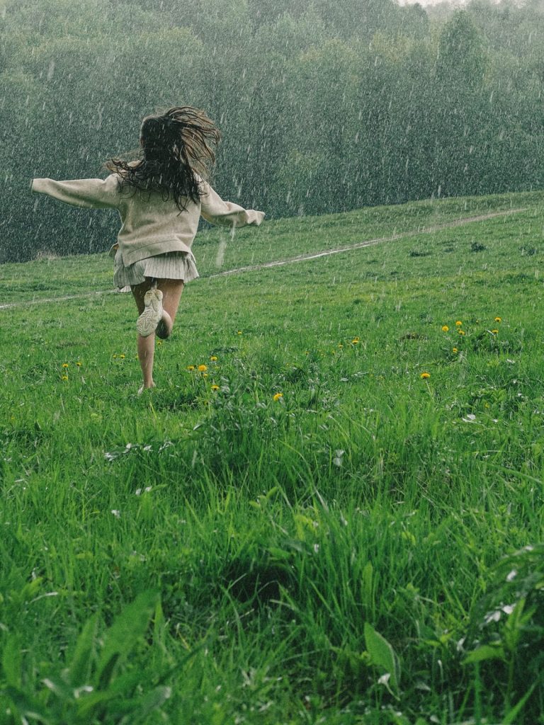 Jeune fille courant sous la pluie dans un pré